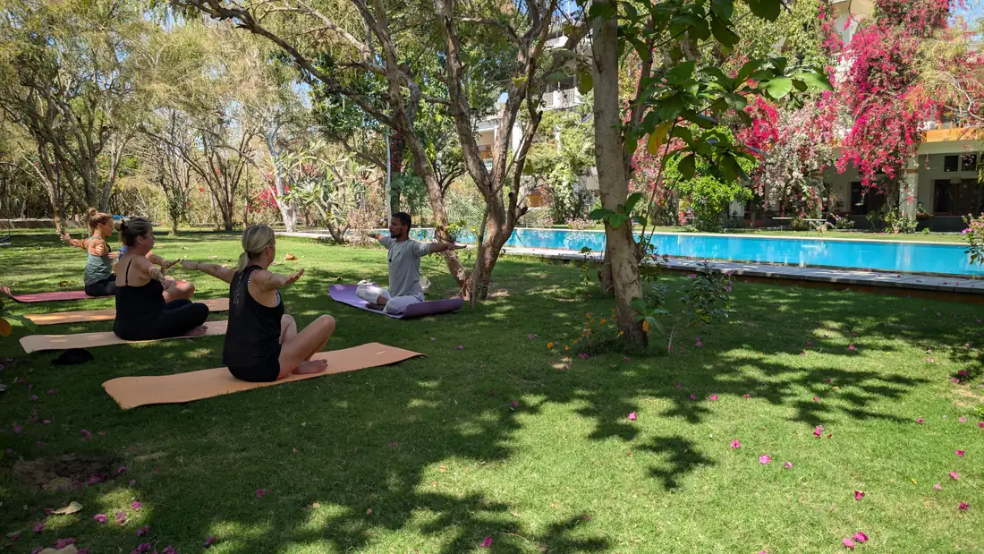 An instructor leading four guests through a yoga session beside the pool