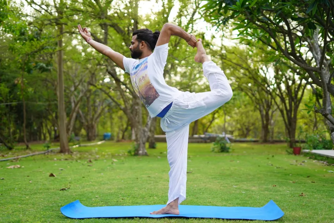 A yoga practitioner balancing in dancer pose on the farm lawn