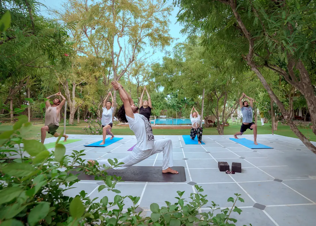 A group yoga class on the deck, pool and gardens behind them